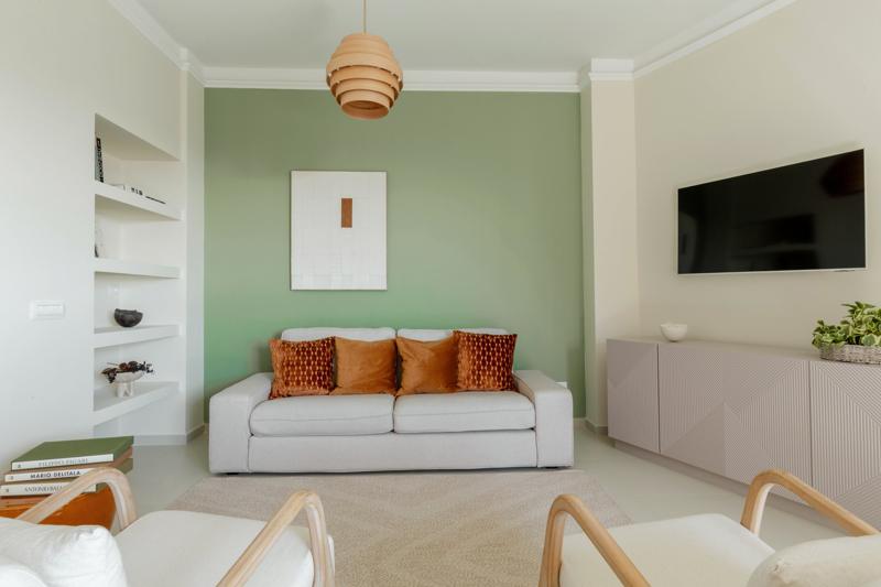 Living room with a sage green wall, sofa with terracotta cushions and two armchairs