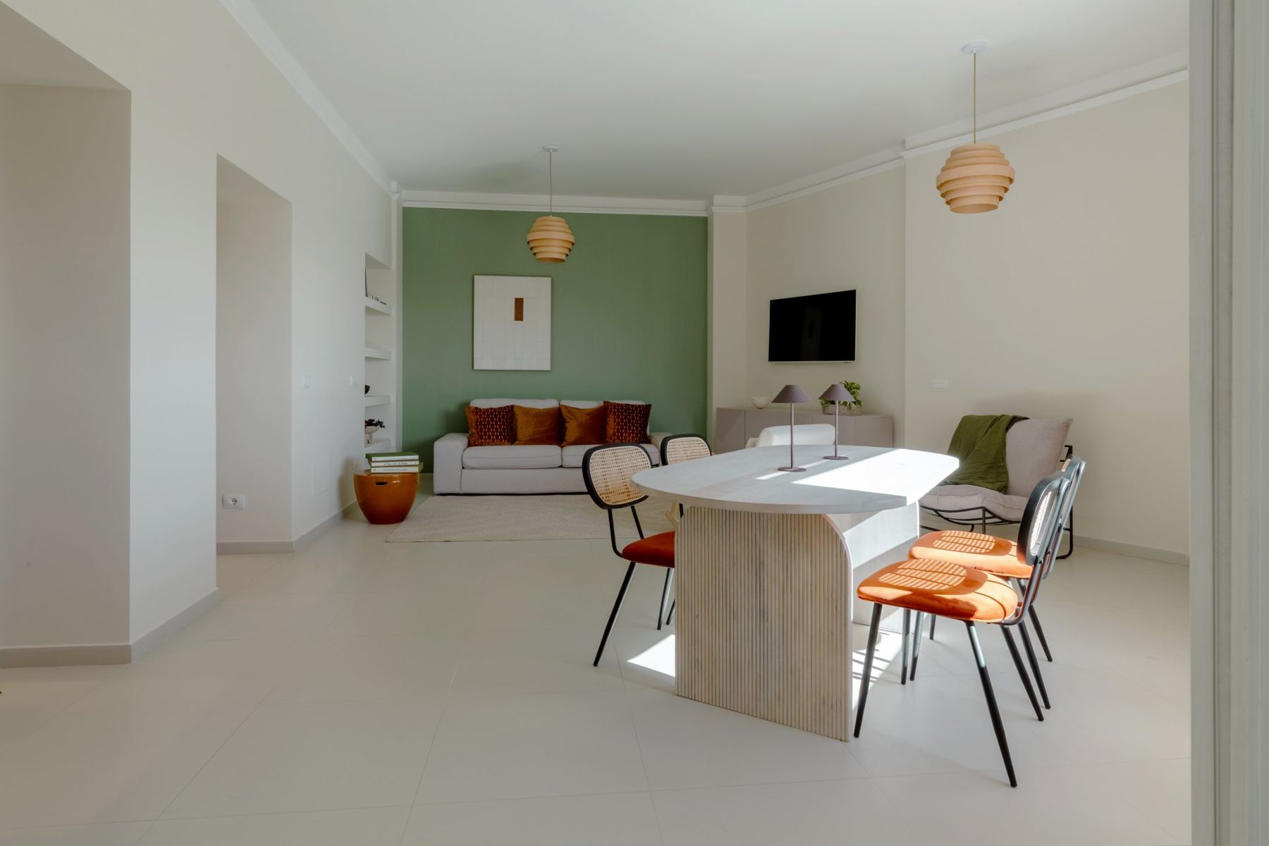 Open living and dining area with a sage green wall, sofa and oval dining table