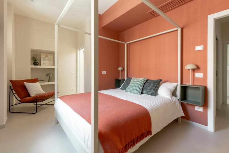 Bedroom with a white four-poster bed against a coral-painted wall