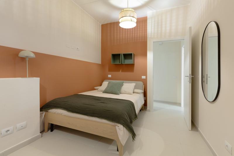 Bedroom with a half-painted coral wall, wooden bed and olive throw