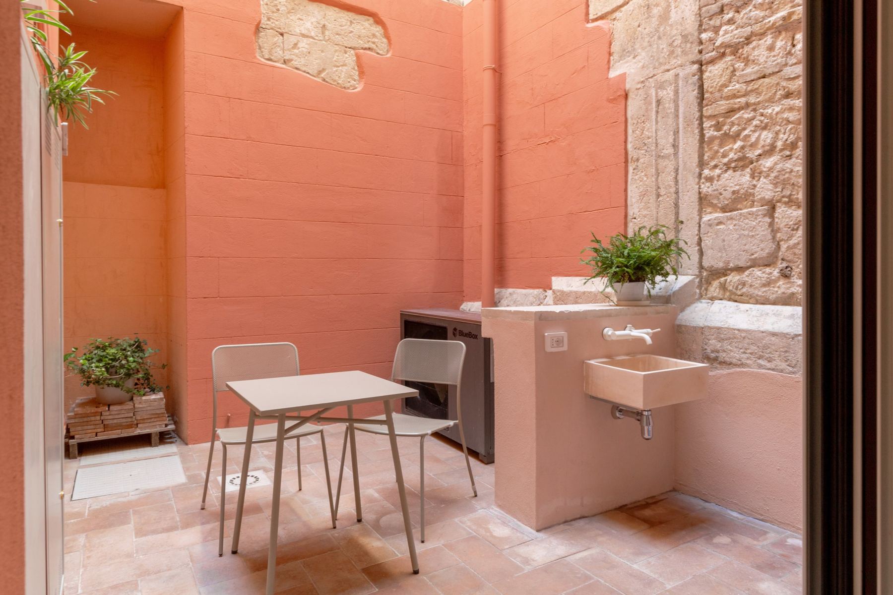 Private courtyard with painted walls, exposed old stone, a small table and a stone sink